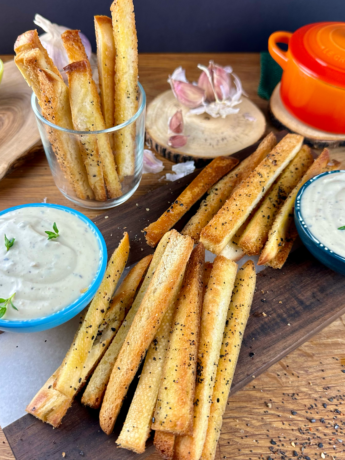 A bowl of creamy roasted garlic dip garnished with fresh herbs, surrounded by toasted bread slices.