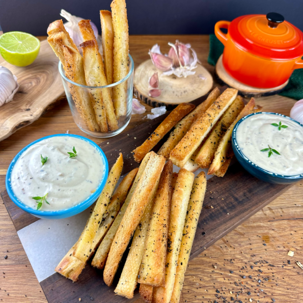 A bowl of creamy roasted garlic dip garnished with fresh herbs, surrounded by toasted bread slices.