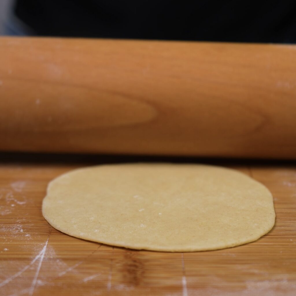 Rolling tortilla dough with a rolling pin on a floured surface