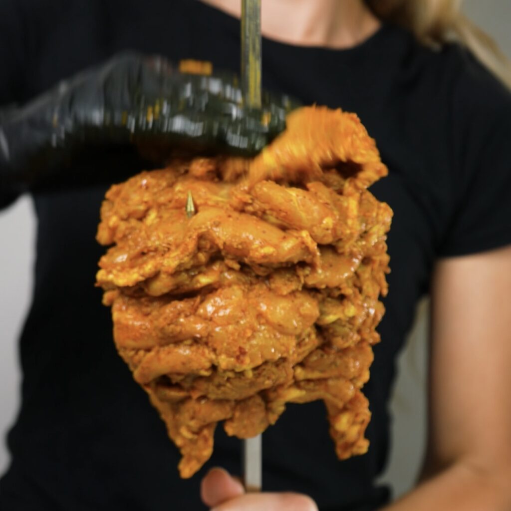 Marinated chicken thighs being skewered tightly onto the JoeTisserie spit.