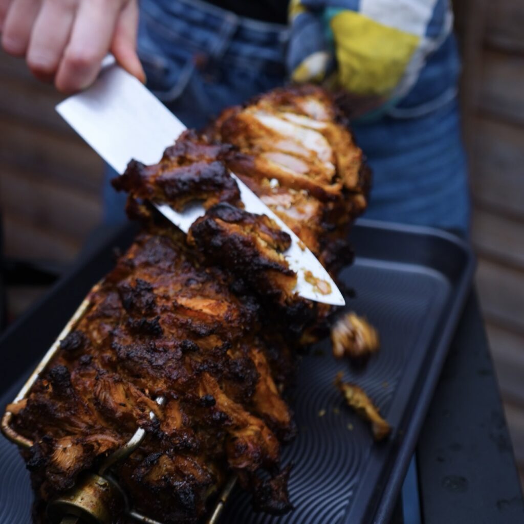 Slicing off the crispy outer layer of Chicken Shawarma from the spit.