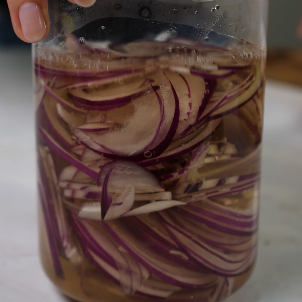 Sliced red onions being pickled in a jar.