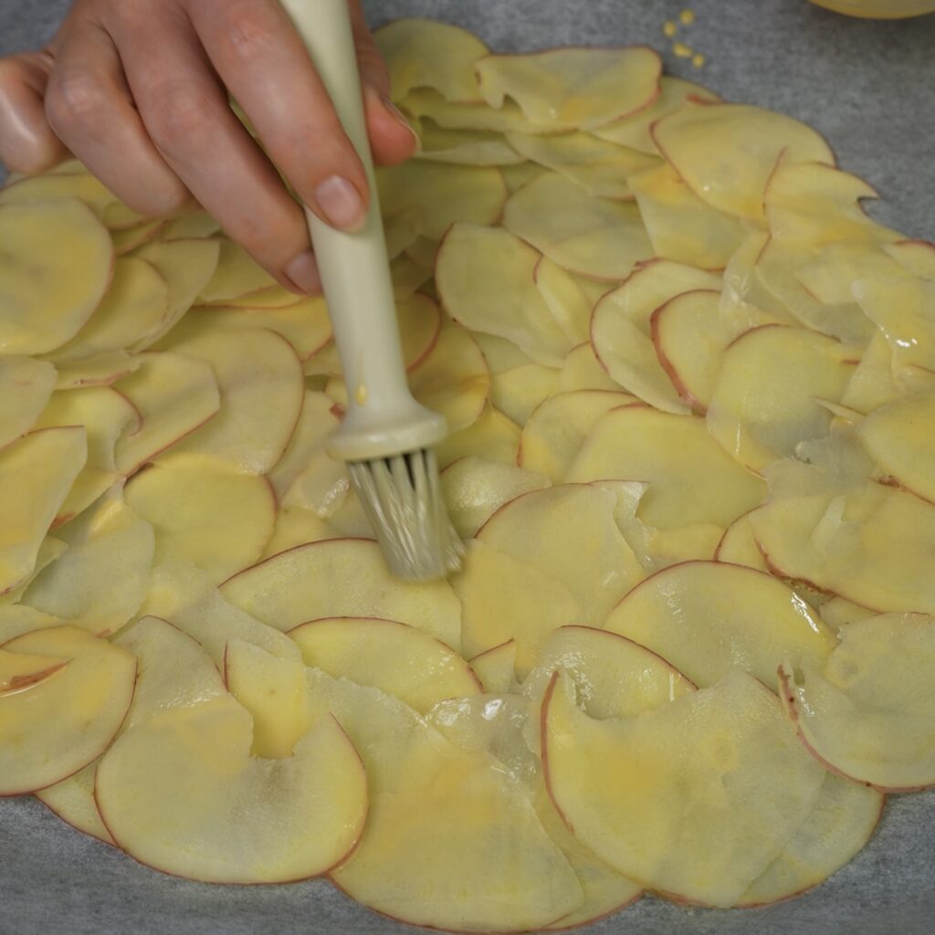 Brushing paper-thin potato slices with egg wash for a crispy potato wrap crust.