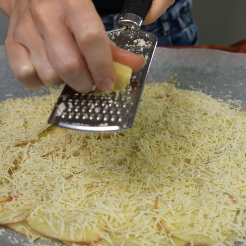 Grating Parmesan cheese over paper-thin potato slices