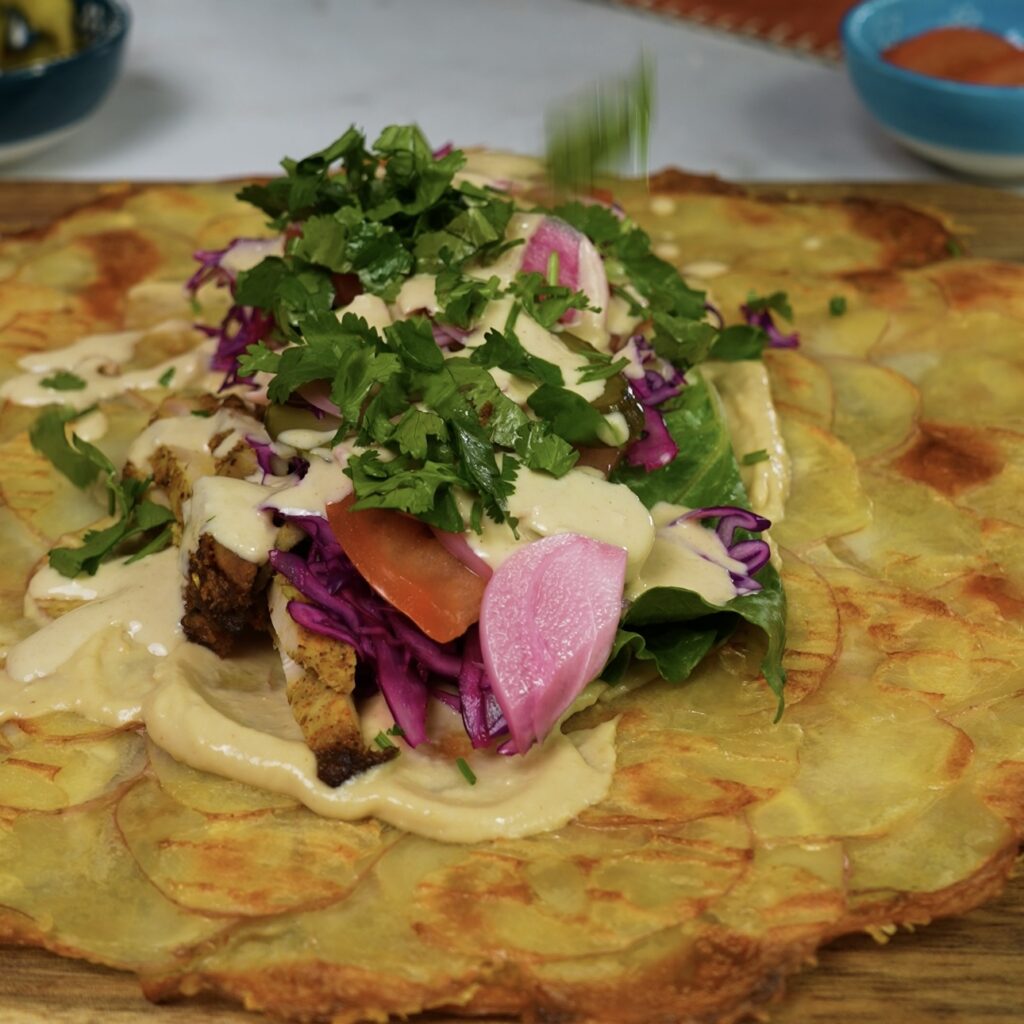 Potato crust topped with a variety of fillings including chicken shawarma, vegetables, and hummus.