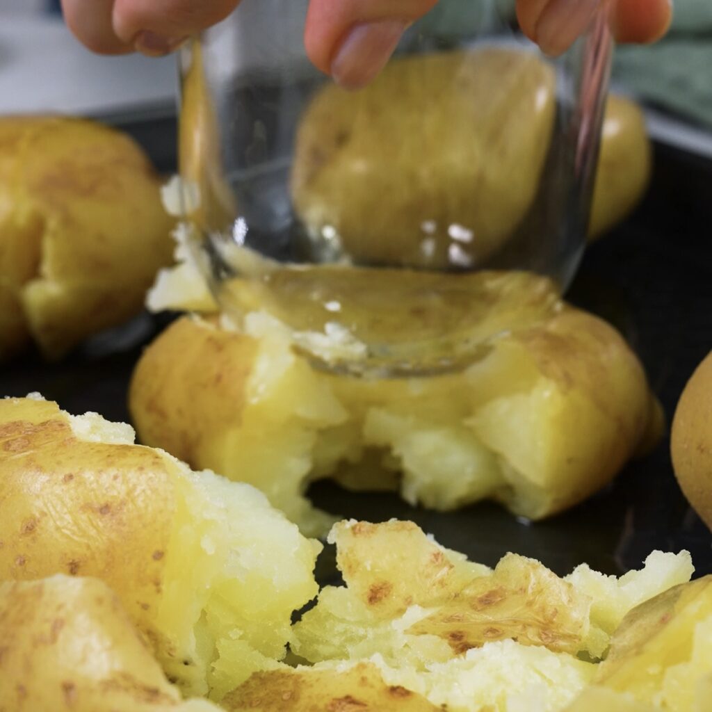 Crushing boiled potatoes with a glass on a baking tray.