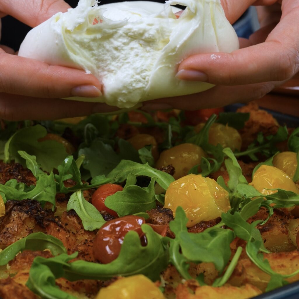 Assembling Loaded Crushed Potatoes with roasted tomatoes, fresh rocket, and burrata.