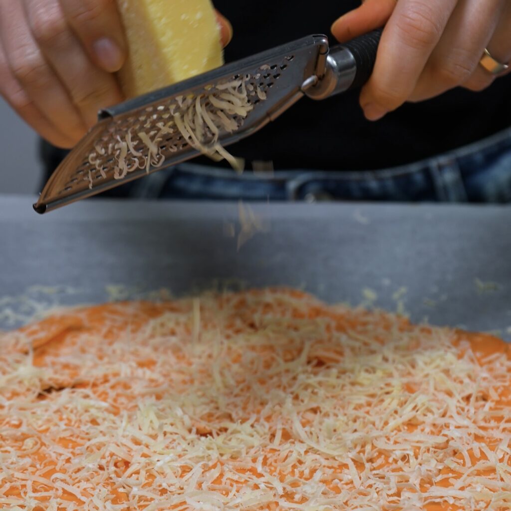 Parmesan being grated over sweet potato slices