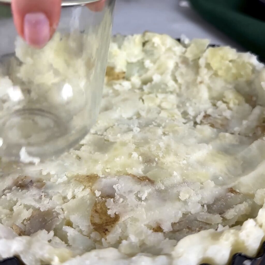 Crushing potatoes with a glass to form pie base