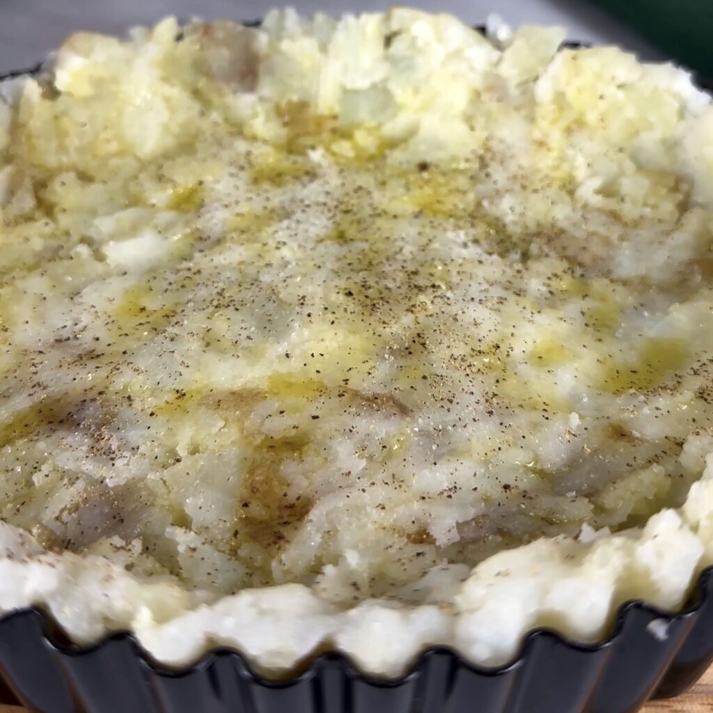 Potato crust drizzled with olive oil, salt, and pepper, ready for baking