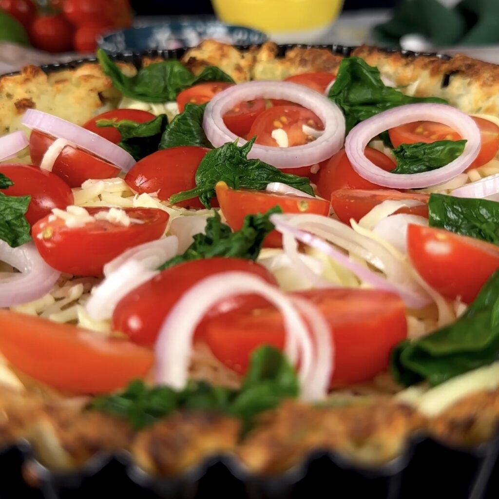 Baked potato crust topped with vegetables, ready for egg mixture