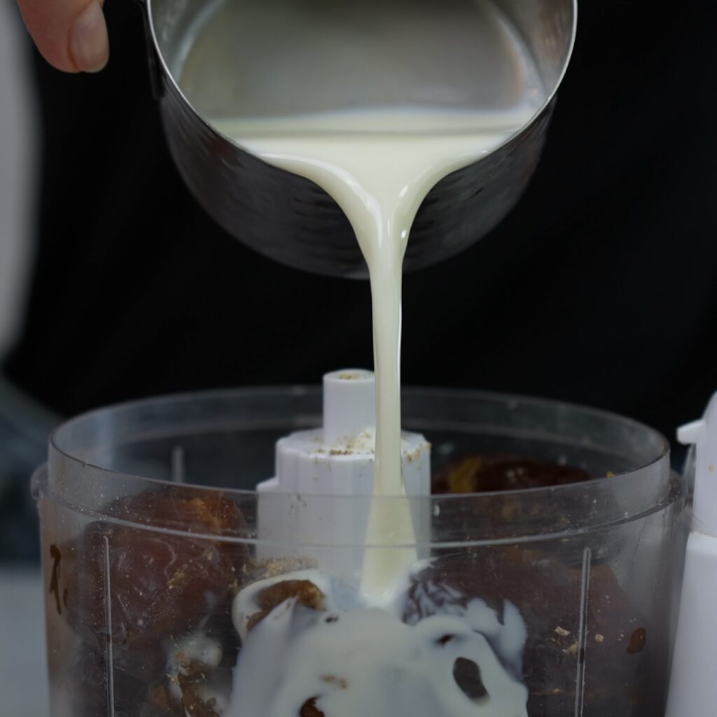 Blending pitted dates, cardamom, and milk into a smooth paste.