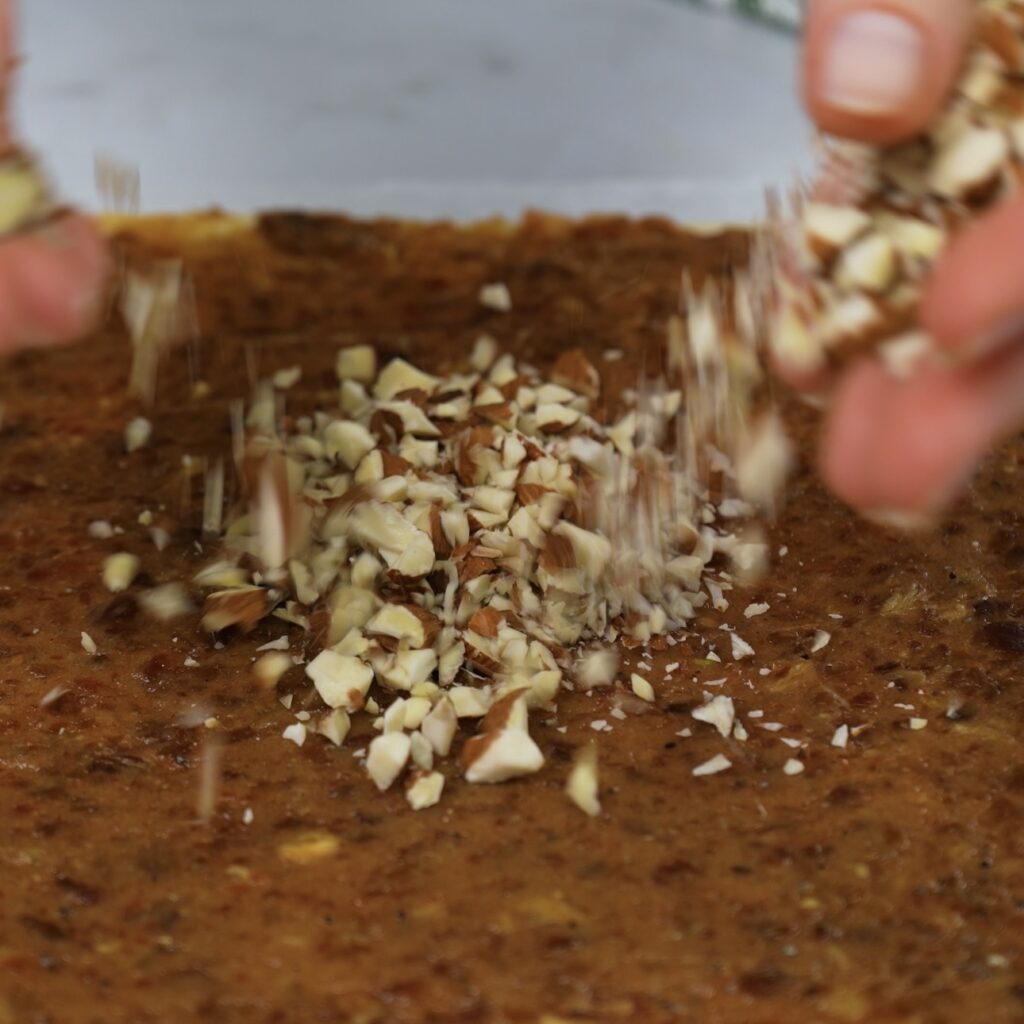 Sprinkling crushed almonds over the date and cardamom paste on puff pastry.