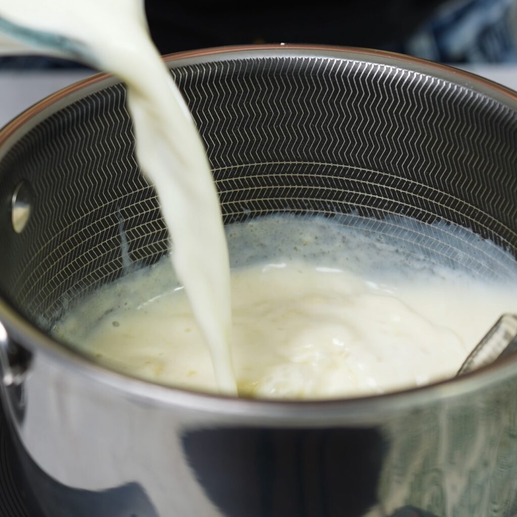 Pouring milk into the roux in a saucepan