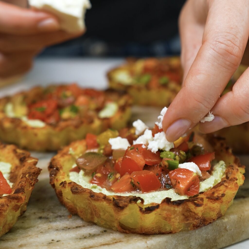 Topping Mini Crushed Potato Tarts with crumbled feta.