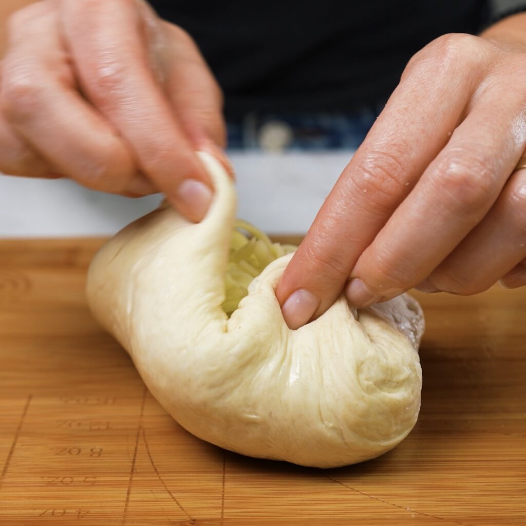 Folding dough edges to seal the mozzarella cheese inside.