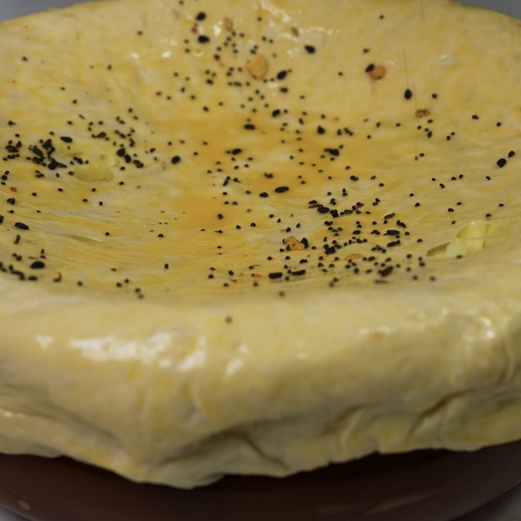 Brushing dough with egg wash and sprinkling sesame seeds.