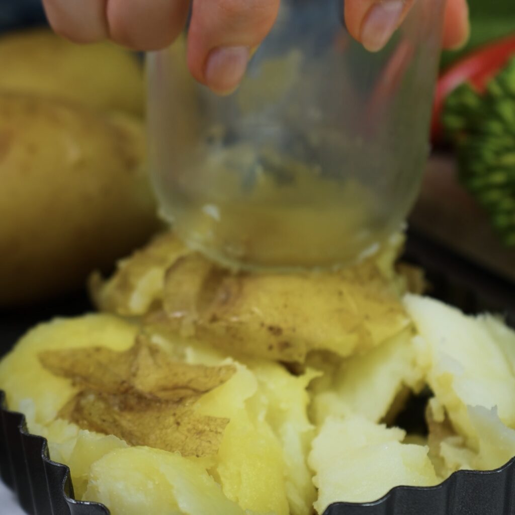 Crushing boiled potatoes in a quiche tin with a glass to form a base for the quiche.