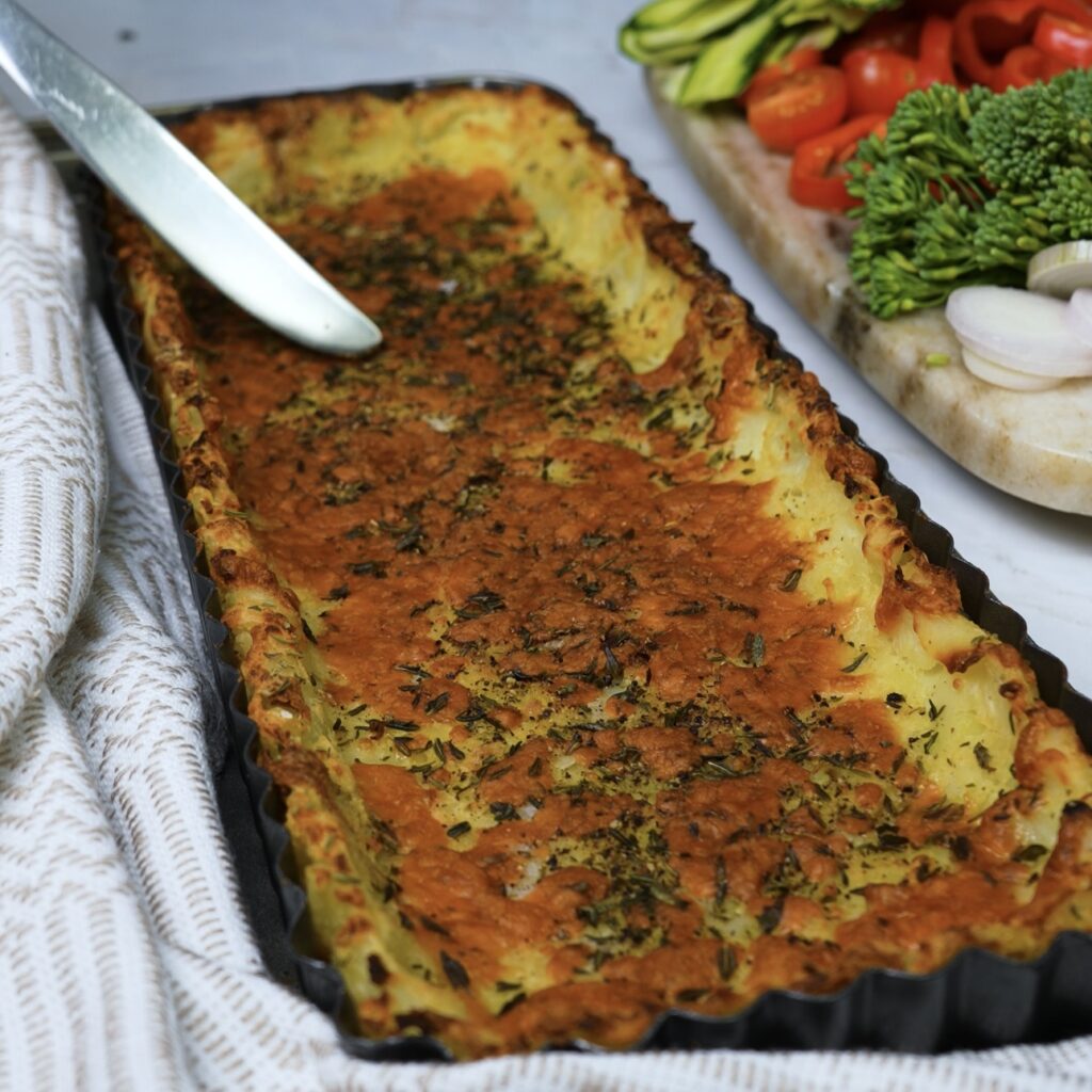 A golden-brown baked potato crust in a quiche tin, ready to be filled with vegetables and custard.