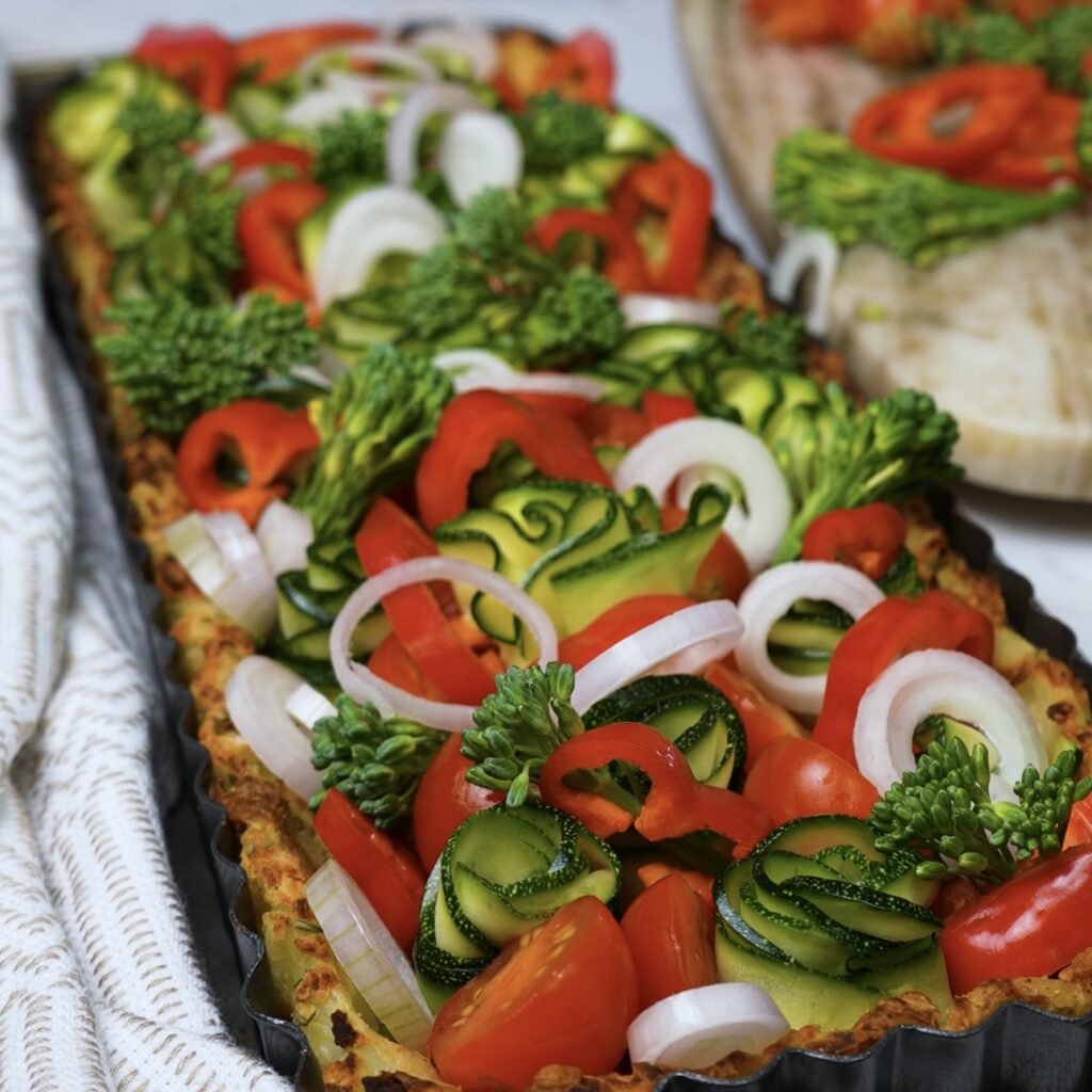 Colourful vegetables arranged neatly in a baked potato crust, ready for the custard filling.