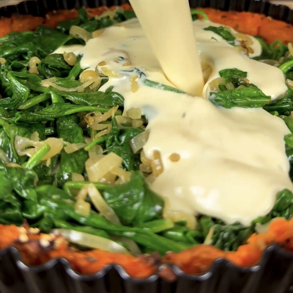 Pouring egg mixture over spinach in sweet potato quiche