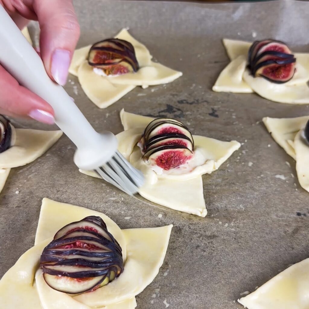 Brushing Fig Puffs with Goat Cheese with egg yolk for a golden finish.