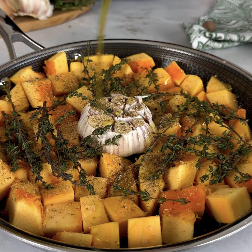 Cubed pumpkin, garlic bulb, and thyme sprigs in a pan, ready for roasting.