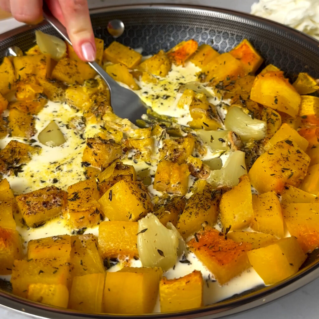 Mashing roasted pumpkin with cream in a pan using a fork