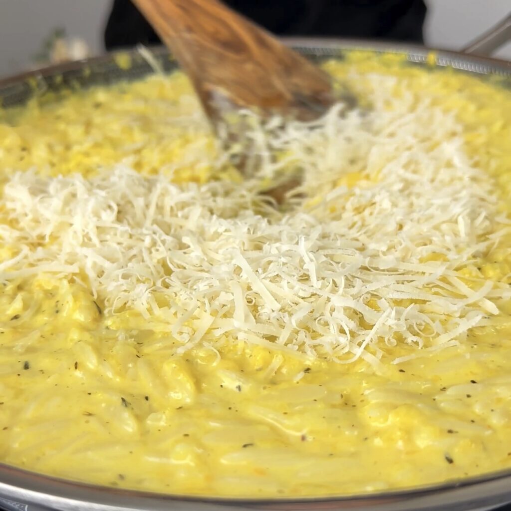 Combining cooked orzo and grated Parmesan cheese with the pumpkin mixture in a pan.