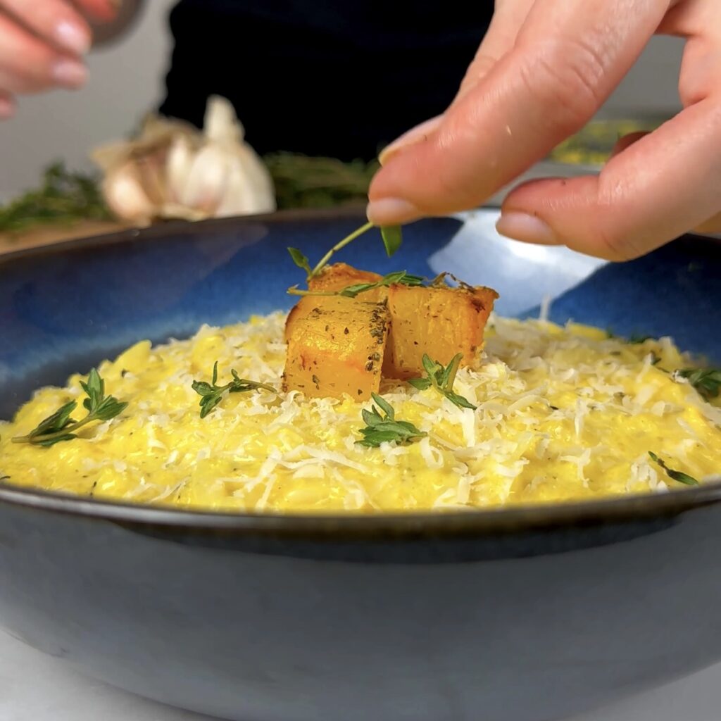 Bowl of creamy roasted pumpkin orzo garnished with thyme and Parmesan cheese.