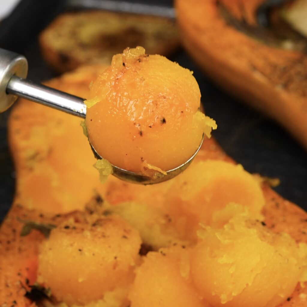 Scooping the roasted flesh from a butternut squash.