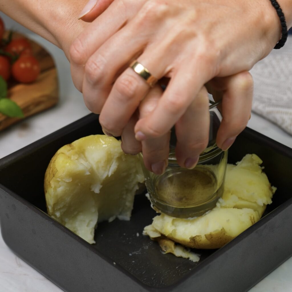 Crushing cooked potatoes with a glass in a greased cake tin for the Crushed Potato Cheesecake