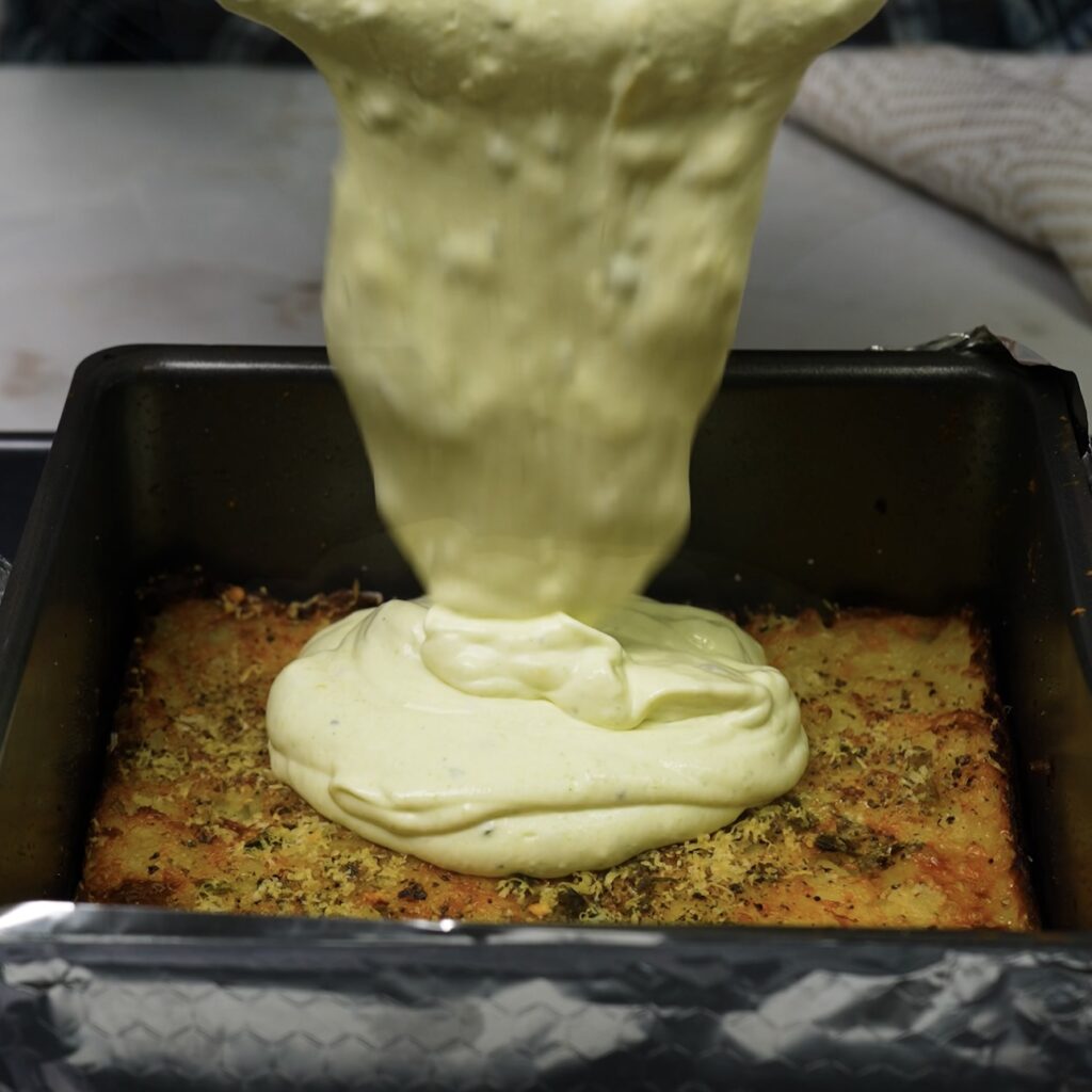 Pouring the creamy filling over the pressed potato base in a cake tin.