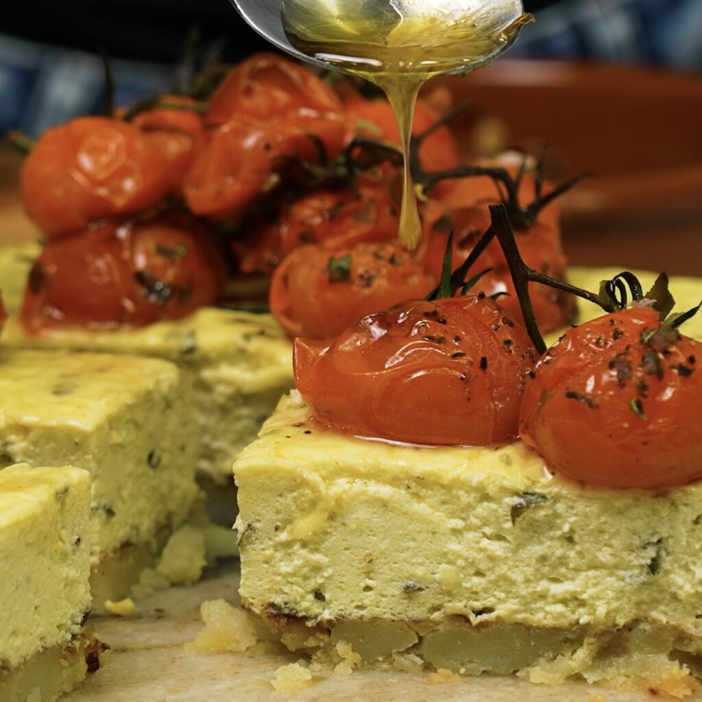 Sliced Savoury Crushed Potato Cheesecake topped with roasted cherry tomatoes.