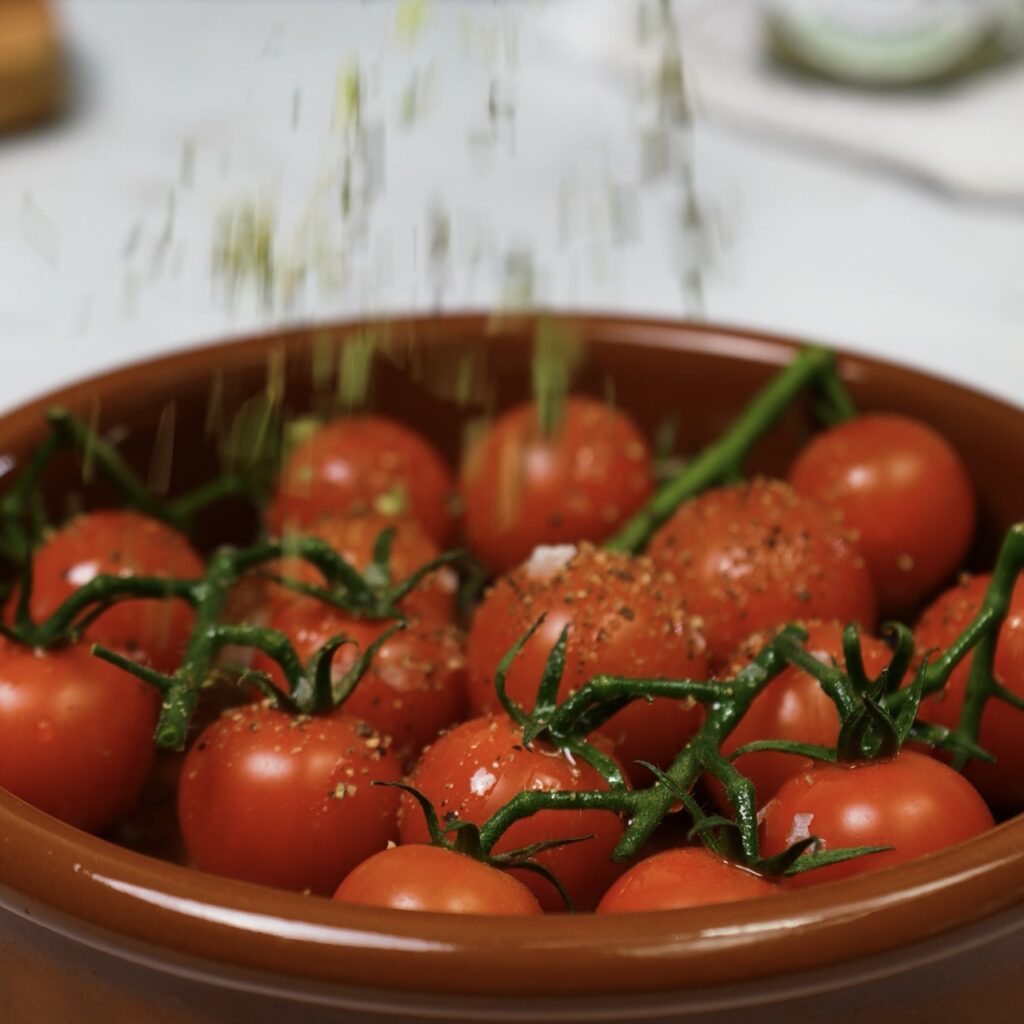 Cherry tomatoes seasoned and arranged on a baking tray, ready for roasting.