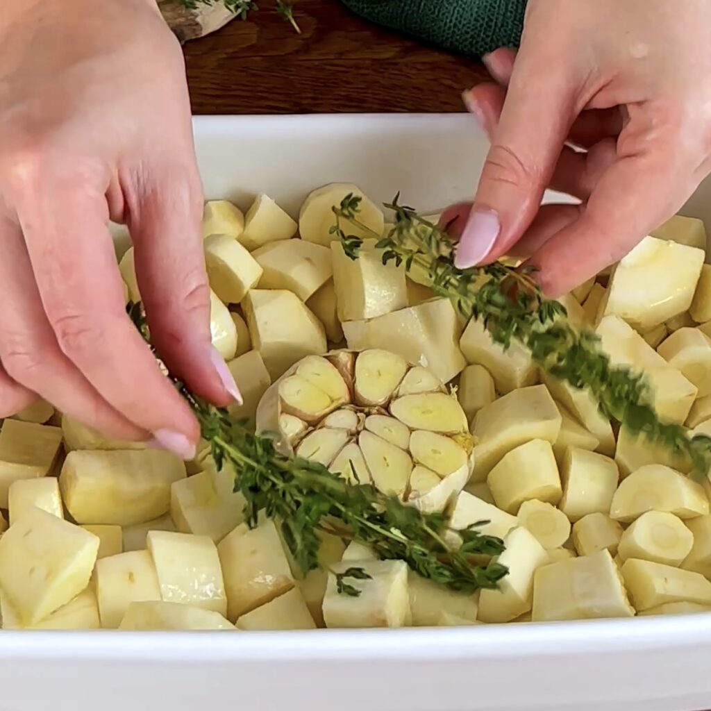 Parsnips, garlic, and thyme arranged in a baking dish, ready for roasting.