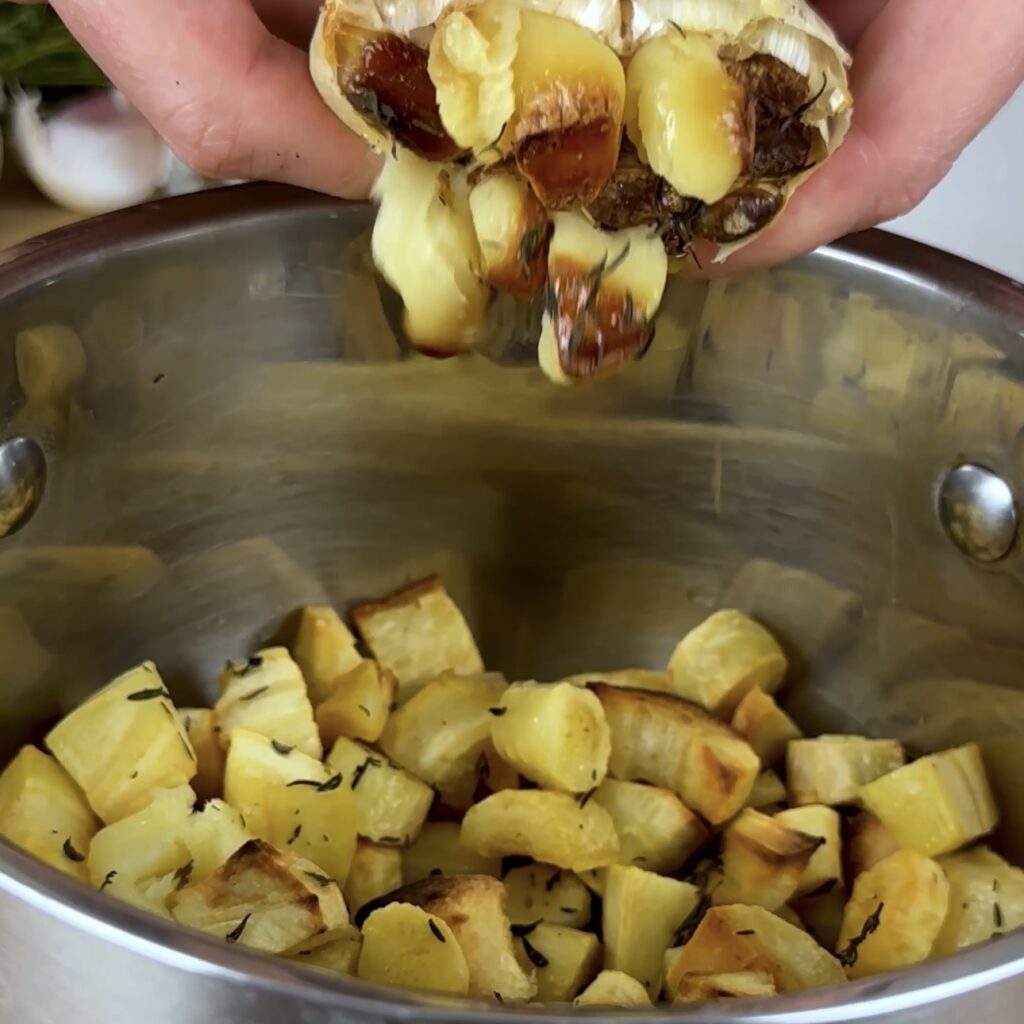 Squeezing roasted garlic into a pot with parsnips