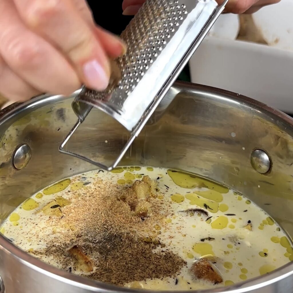 Grating nutmeg into a pot filled with ingredients for Roasted Parsnip Soup.