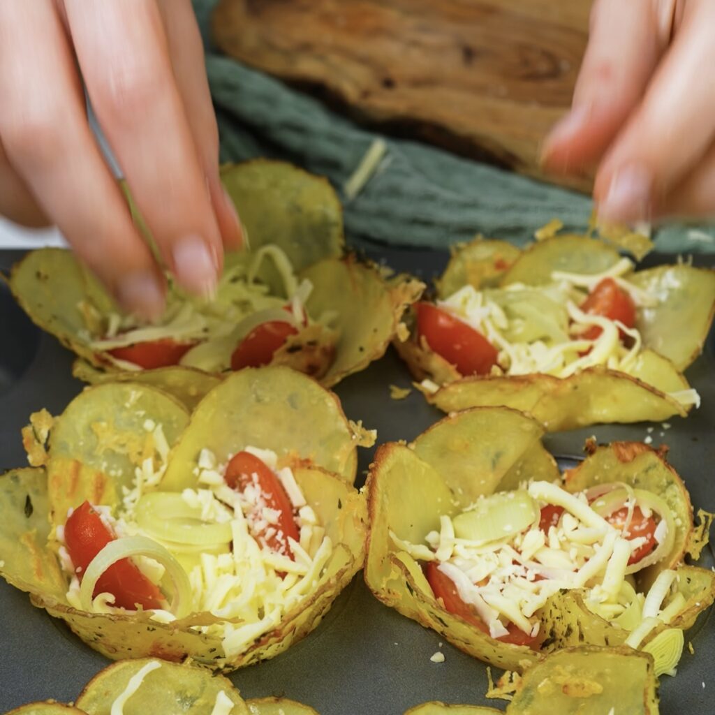 Potato cups filled with cheese and fresh vegetables, ready to be baked.