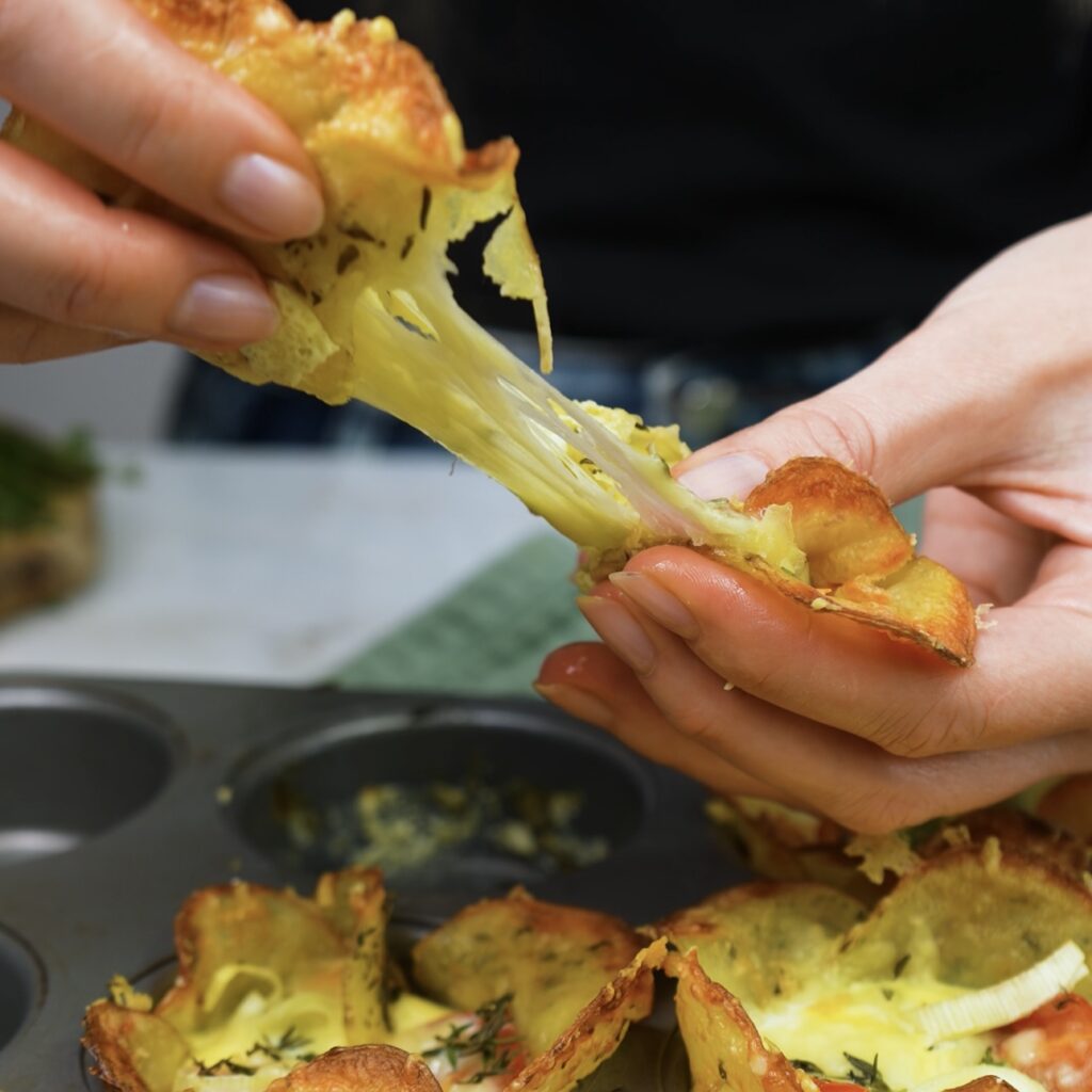 Cheese pull from baked potato cups filled with veggies, showcasing gooey melted cheese.