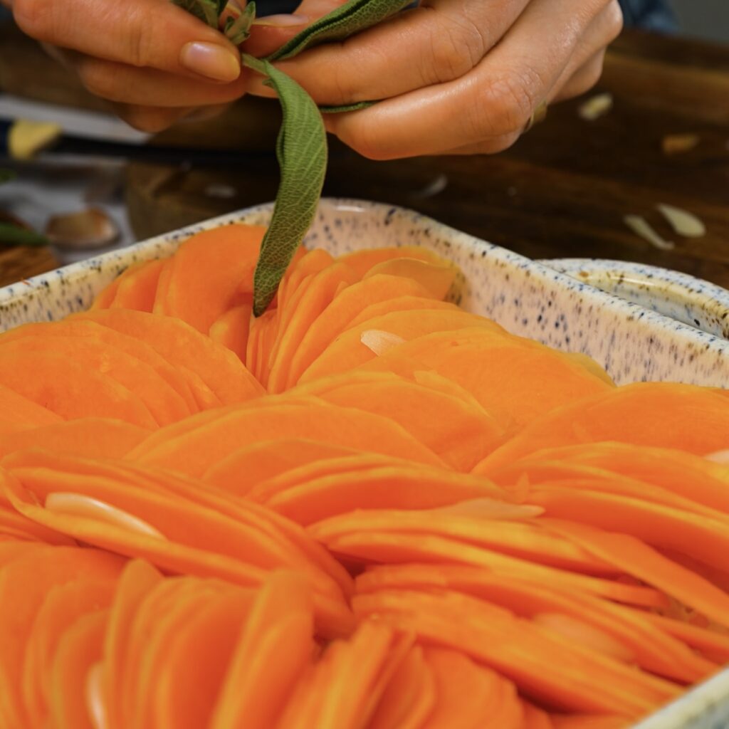 Adding fresh sage leaves to the assembled butternut squash gratin.