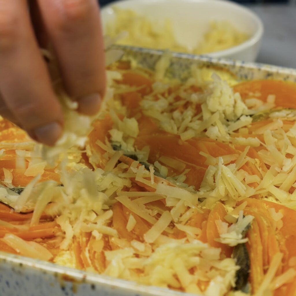 Sprinkling grated cheese over the assembled butternut squash gratin.