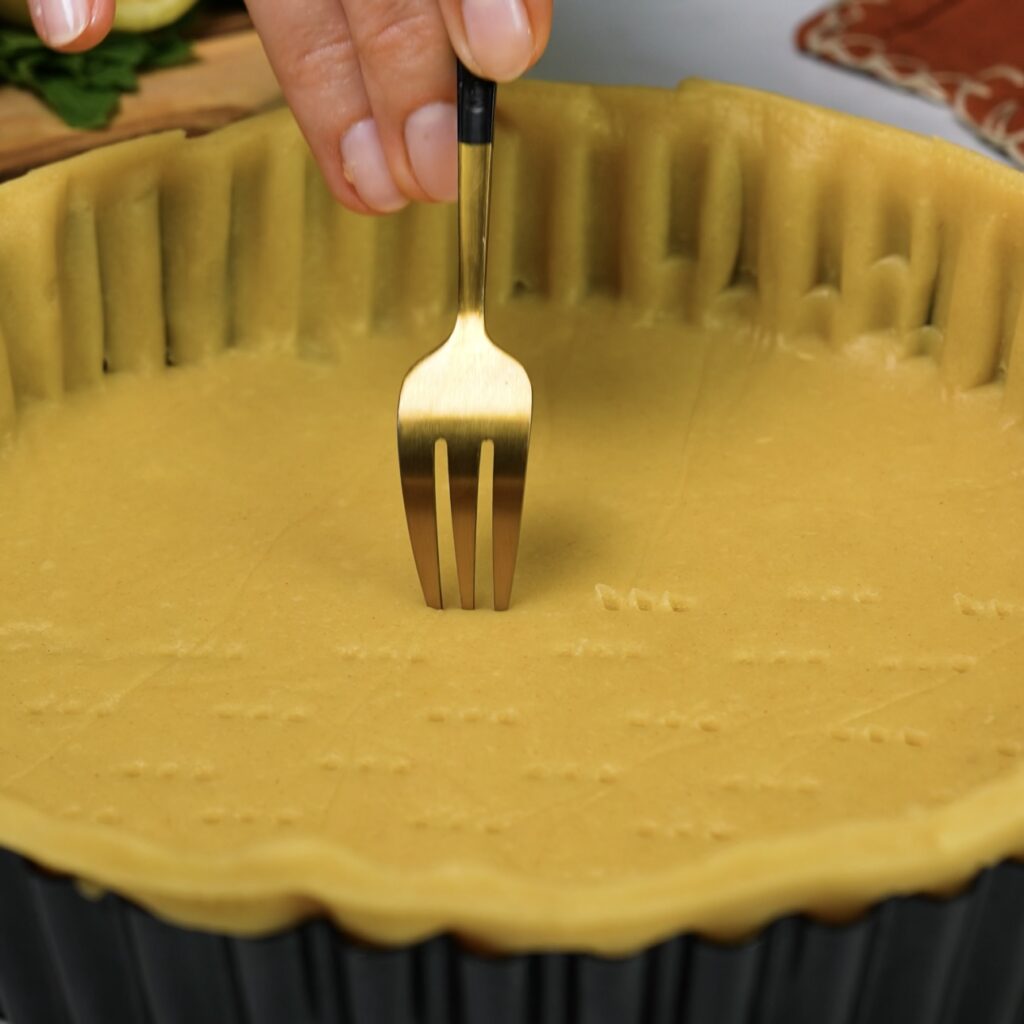 Pricking the tart base with a fork before baking.