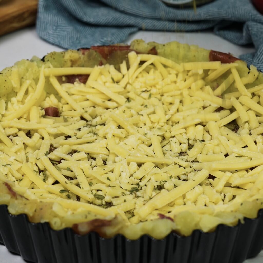 Crushed potatoes in a tart tin forming a rustic crust for Cottage Pie, topped with melted cheese and garnished with fresh rosemary.