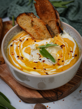 A bowl of Roasted Butternut Squash and Pear Soup topped with crumbled Gorgonzola cheese and a drizzle of olive oil, served with crusty bread on the side.