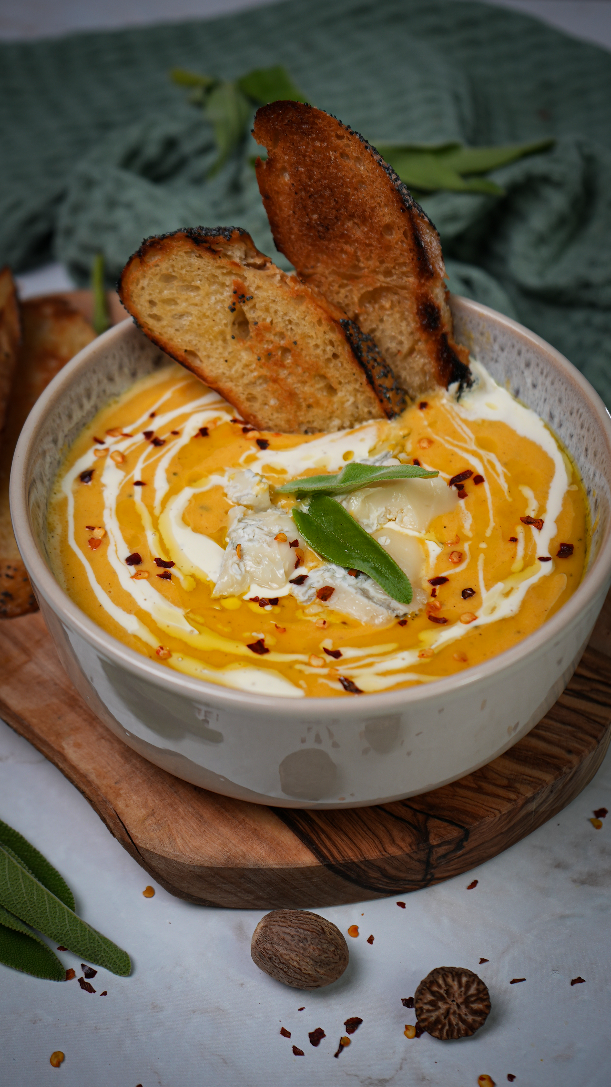 A bowl of Roasted Butternut Squash and Pear Soup topped with crumbled Gorgonzola cheese and a drizzle of olive oil, served with crusty bread on the side.