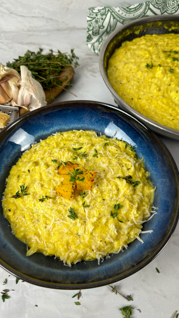 Bowl of creamy roasted pumpkin orzo garnished with thyme and Parmesan cheese.