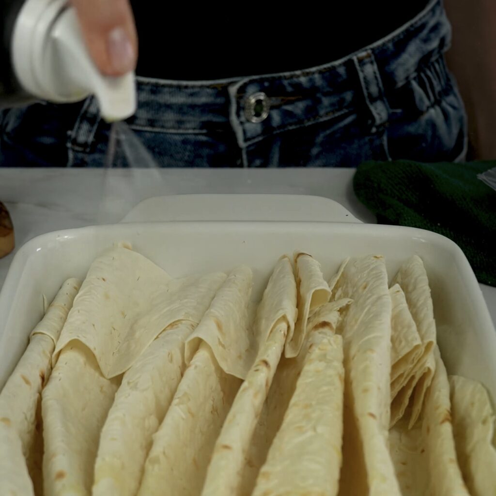 Spraying olive oil onto lavash bread in a baking dish.