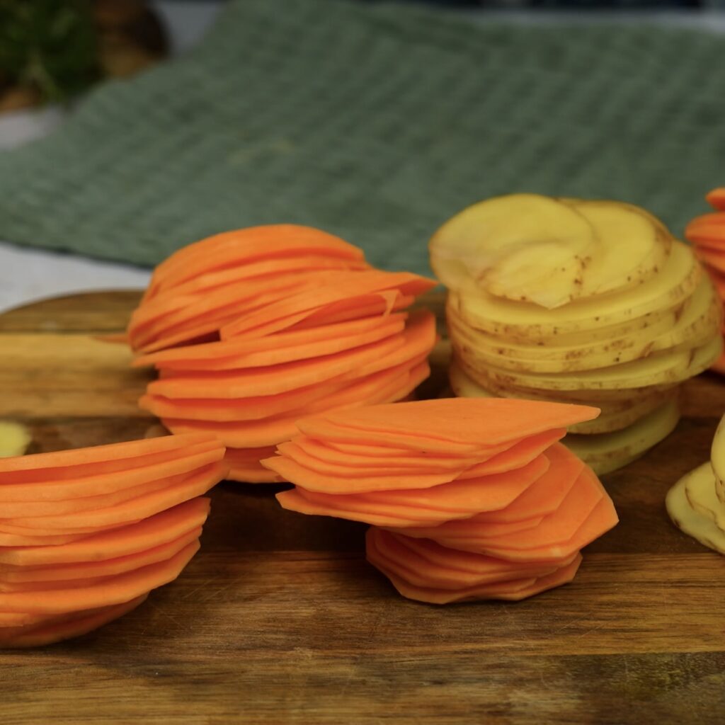 Sliced sweet and regular potatoes resting on a cutting board.