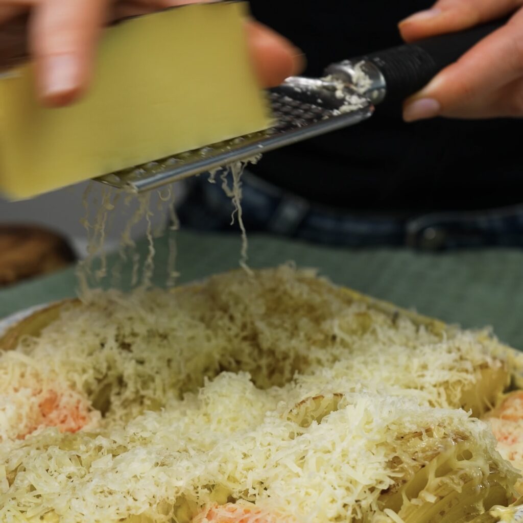 Grating cheese over prebaked sweet and regular potatoes in a baking dish.